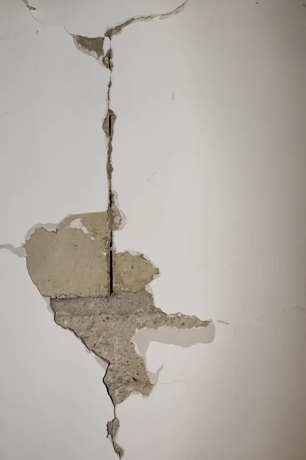 Fissure verticale ouverte dans l’enduit d’un mur de maison